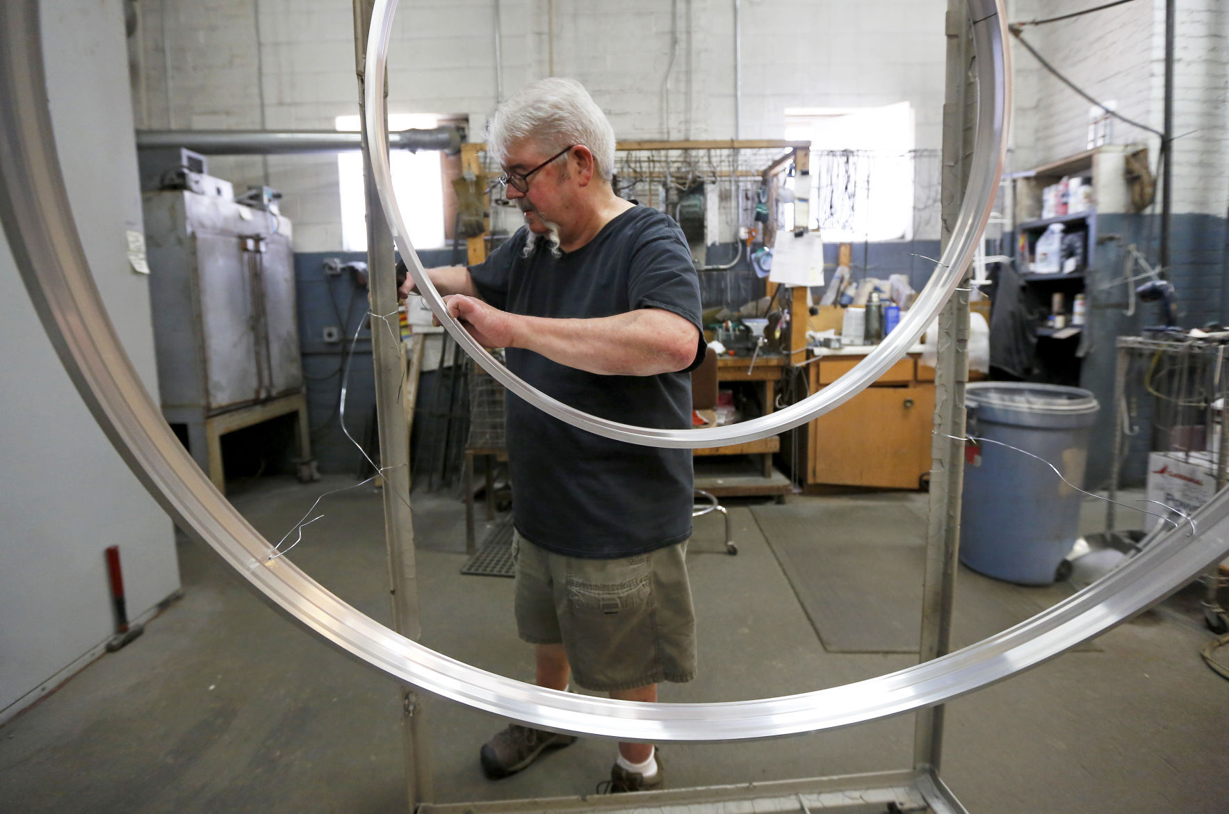 Jim Walch hangs light fixture rims before painting at Fire Farm Lighting. The Elkader, Iowa, business creates custom lighting, with many orders in low numbers. As a result, the company adjusts and figures out ways to fill the requests.Video: TelegraphHerald.com PHOTO CREDIT: EILEEN MESLAR