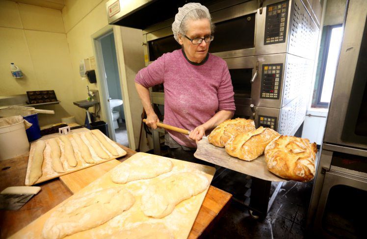 Georgia Mihalakis removes ciabatta bread from the oven at Millwork Bakery. Through the years, she’s been in different downtown Dubuque locations with her businesses, which had a connection to baked goods. In 2017, she made the White Street site the focal point.    PHOTO CREDIT: JESSICA REILLY