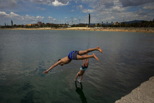 Two boys jump from a breakwater into the water in Barcelona, Spain, Wednesday, June 17, 2020. Spanish Prime Minister Pedro Sanchez has announced a state ceremony to be held on July 16 to honour more than 27,000 who have died for the coronavirus. The ceremony will be held four months after Spain imposed one of the strictest lockdowns in the world to respond to the virulent cluster that followed major outbreaks in China and northern Italy. (AP Photo/Emilio Morenatti) PHOTO CREDIT: Emilio Morenatti
