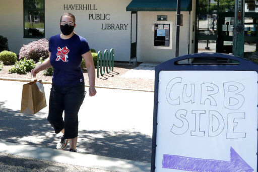 Librarian Emily Giguere delivers books to a reader waiting in his car outside the Haverhill Library, Wednesday, June 17, 2020, in Haverhill, Mass. Libraries are closed for interior use due to coronavirus concerns. (AP Photo/Elise Amendola) PHOTO CREDIT: Elise Amendola