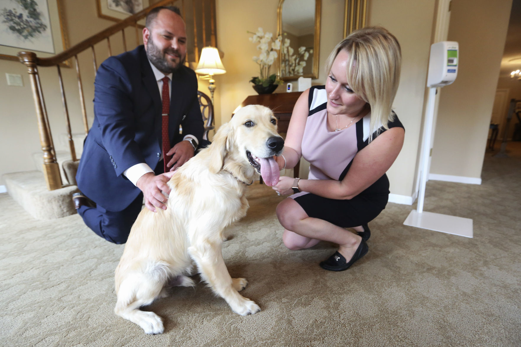 Managing Funeral Director Scott Glover and Office Manager Samantha Glover play with their dog, Stanley, at Hoffmann Schneider & Kitchen Funeral Home and Cremation Service in Dubuque on Friday. Stanley is an English golden retriever and comes to the business to provide stress relief for employees and visitors. PHOTO CREDIT: NICKI KOHL