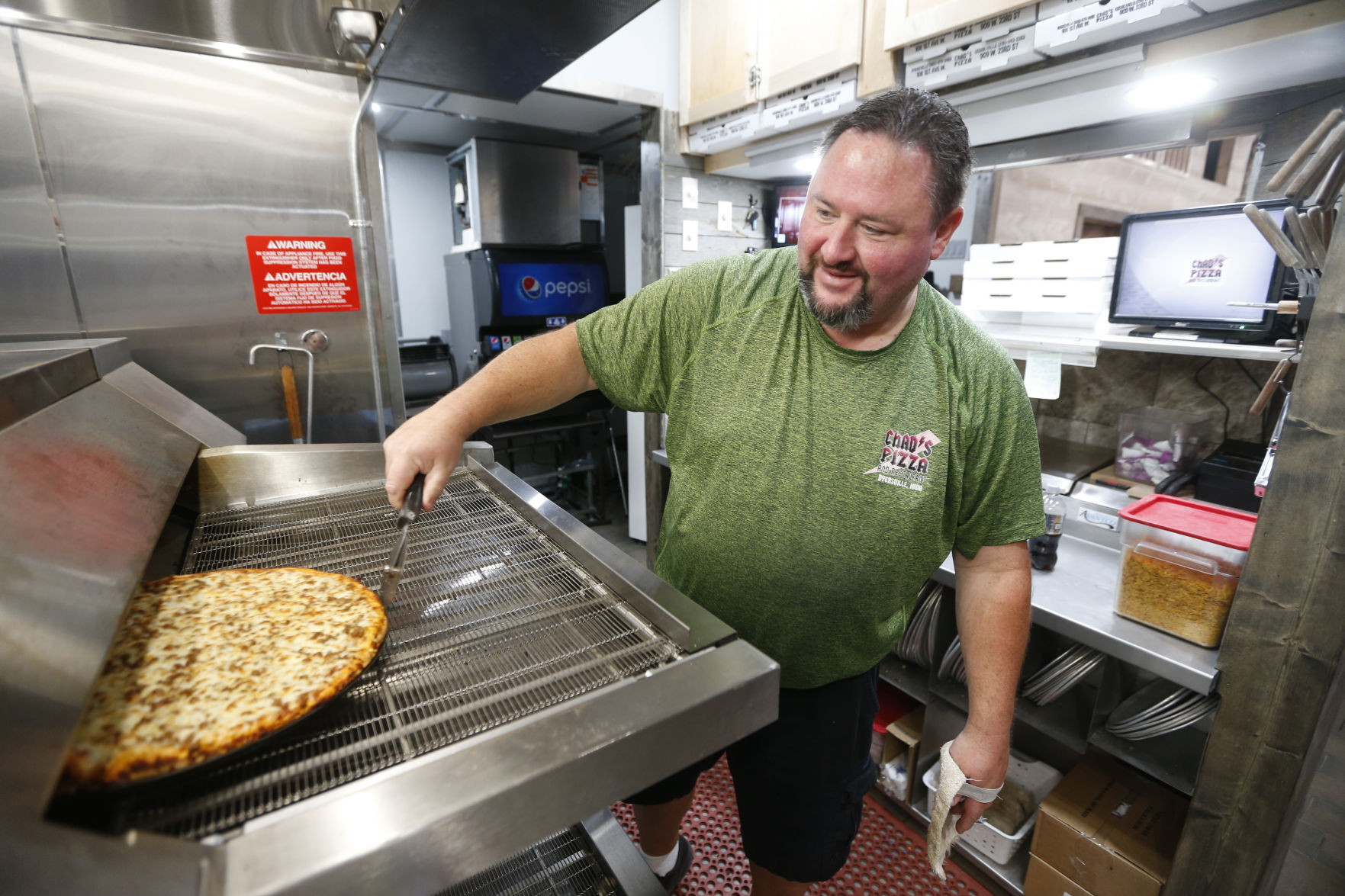 Chad’s Pizza owner Chad Clouse checks a pizza Friday in his new oven that is part of the Dyersville, Iowa, restaurant’s renovation. Clouse said the project will be finished and the dining room reopened in mid-August. PHOTO CREDIT: Dave Kettering