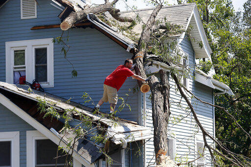 Mike Jacobis pushes a portion of tree trunk away as a neighbor helps on the ground in northwest Cedar Rapids, Iowa, on Wednesday, Aug. 12, 2020. The tree, which fell in Monday