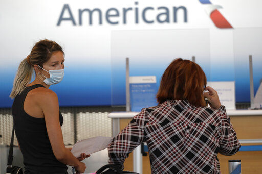 FILE - In this June 16, 2020 photo, travelers wear mask as they wait at the American Airlines ticket counter in Terminal 3 at O