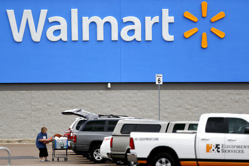 FILE - In this March 31, 2020 file photo, a woman pulls groceries from a cart to her vehicle outside of a Walmart store in Pearl, Miss. Walmart will require customers to wear face coverings at all of its namesake and Sam
