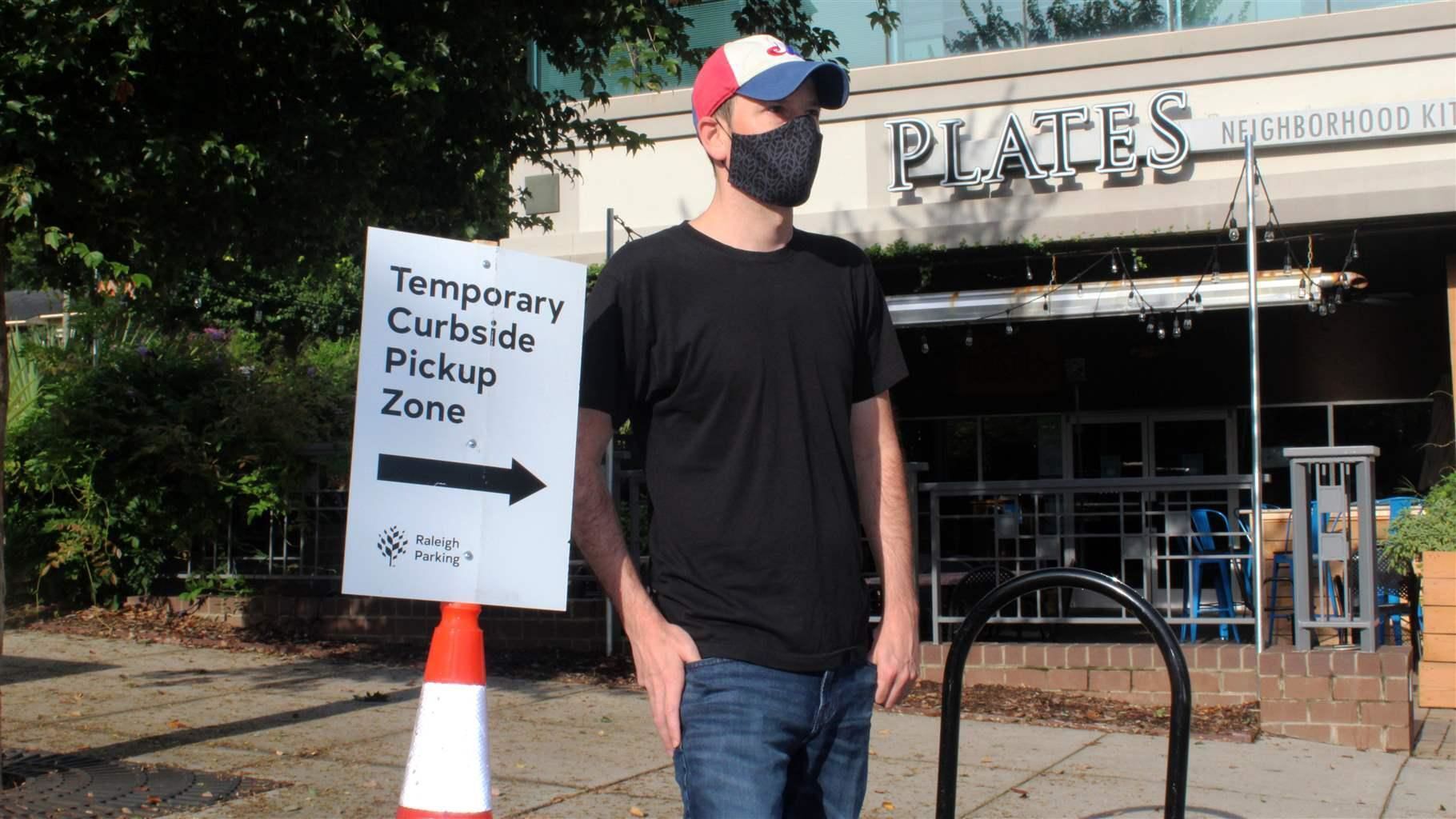 Justin Gallus stands near a curbside pickup zone outside his Plates Neighborhood Kitchen restaurant in downtown Raleigh, N.C., this week. Cities and counties are creating these spaces to help keep restaurants in business during the COVID-19 outbreak. PHOTO CREDIT: Tribune News Service