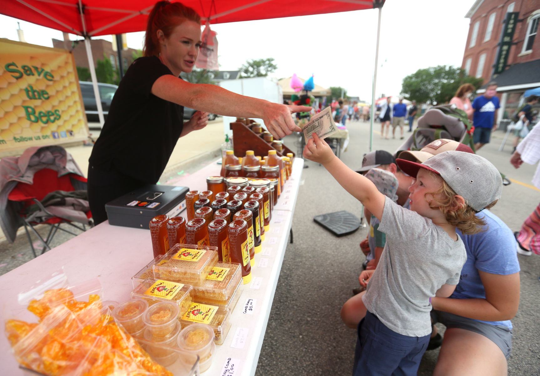 Joy Schultz, with Little Red’s Honey Farm in Reedsburg, Wis., takes money from Lexton Moeller, and his mom, Kaytlan Moeller, both of Asbury, Iowa, during Dubuque Farmers Market in downtown Dubuque on Saturday. PHOTO CREDIT: JESSICA REILLY