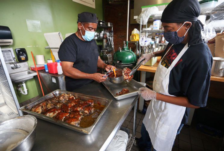 Allen Sutton (left) and Flo Winfrey prepare Jamaican jerk chicken at Milk House Artisan Eatery, Baked Goods & Catering. Since it expanded its menu, the venue also offers indoor and outdoor seating for patrons. PHOTO CREDIT: NICKI KOHL