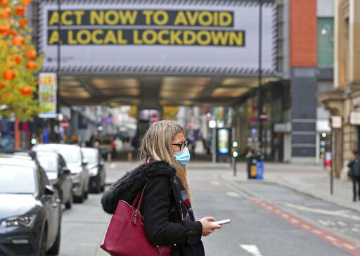 A woman wearing a face mask walks in Manchester, England. The number of confirmed COVID-19 cases across the planet has surpassed 40 million, but experts say that is only the tip of the iceberg when it comes to the true impact of the pandemic that has upended life and work around the world. PHOTO CREDIT: Peter Byrne
