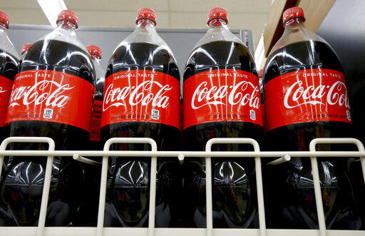 FILE- In this Aug. 8, 2018, file photo bottles of Coca-Cola sit on a shelf in a market in Pittsburgh. The Coca-Cola Co. said on Thursday, Oct. 22, 2020, it saw gradual improvement in the third quarter, as it turned its focus to emerging leaner from the global pandemic. Atlanta-based Coke said its revenue fell 9% to $8.7 billion. (AP Photo/Gene J. Puskar, File) PHOTO CREDIT: Gene J. Puskar