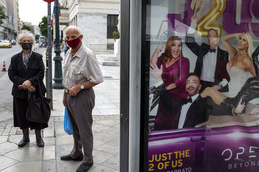 Two people wearing face masks to prevent the spread of COVID-19, wait at a bus station where an advertisement for a TV show is displayed, in Athens, Monday, Nov. 2, 2020. The government announced new lockdown measures Saturday to stem the rapid rise in new cases, among which are the closure of bars, cafes, restaurants and gyms in large swaths of the country, will take effect Tuesday through at least the end of November. (AP Photo/Yorgos Karahalis) PHOTO CREDIT: Yorgos Karahalis
