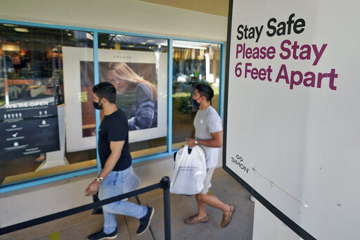 Shoppers wear protective face masks as they walk past a social distancing sign at the Ellenton Premium Outlet stores Friday, Nov. 27, 2020, in Ellenton, Fla. Attendance at the mall was down in an attempt to avoid spreading the corona virus. (AP Photo/Chris O