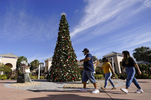 Shoppers wear protective face masks as they walk past a Christmas setting at the Ellenton Premium Outlet stores Friday, Nov. 27, 2020, in Ellenton, Fla. Attendance at the mall was down in an attempt to avoid spreading the corona virus. (AP Photo/Chris O