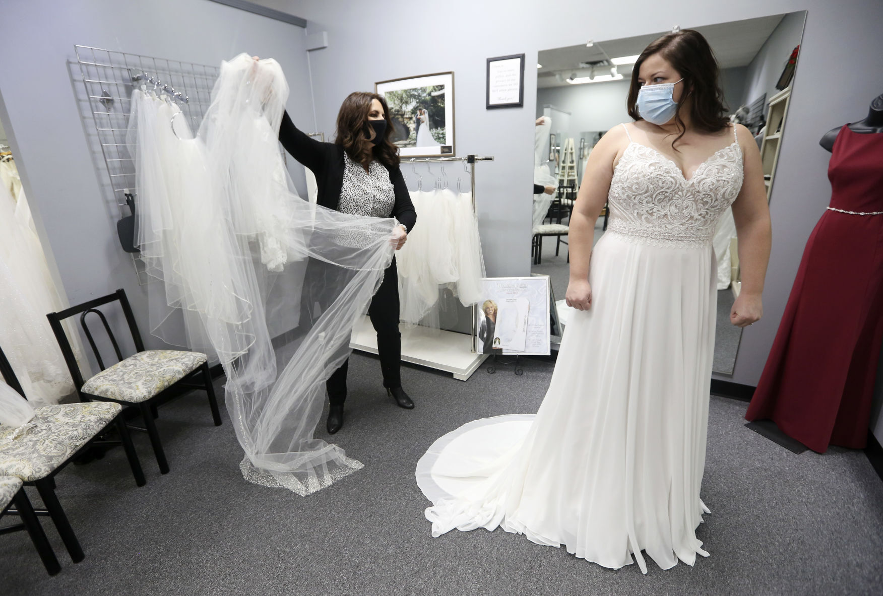 Owner Sherrie Keating (left) assists Ally O’Rourke, of Dubuque, as she tries on bridal dresses and accessories at Cheryl-Ann Bridals & Tuxedos in Dubuque on Tuesday. Engaged couples are look forward to the new year. PHOTO CREDIT: NICKI KOHL