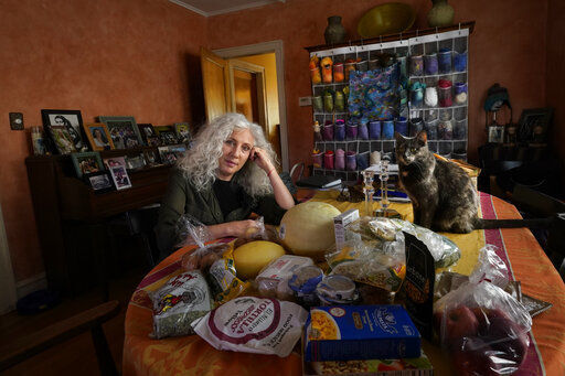 Phyllis Marder poses with her cat, Nellie, with food she recently obtained from a local food bank in the dining room of her home in Evanston, Ill. Now, in the pandemic of 2020, with illness, job loss and business closures, millions more Americans are worried about empty refrigerators and barren cupboards. Food banks are doling out meals at a rapid pace and an Associated Press data analysis found a sharp rise in the amount of food distributed compared with last year.  PHOTO CREDIT: Charles Rex Arbogast