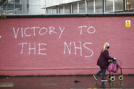 A woman walks past graffiti with the words Victory to the NHS (National Health Service) on a wall at the Royal Victoria Hospital, one of several hospitals around Britain that are handling the initial phase of a COVID-19 immunization program, in West Belfast, Northern Ireland, Tuesday, Dec. 8, 2020. British health authorities rolled out the first doses of a widely tested and independently reviewed COVID-19 vaccine Tuesday, starting a global immunization program that is expected to gain momentum as more serums win approval. (AP Photo/Peter Morrison) PHOTO CREDIT: Peter Morrison