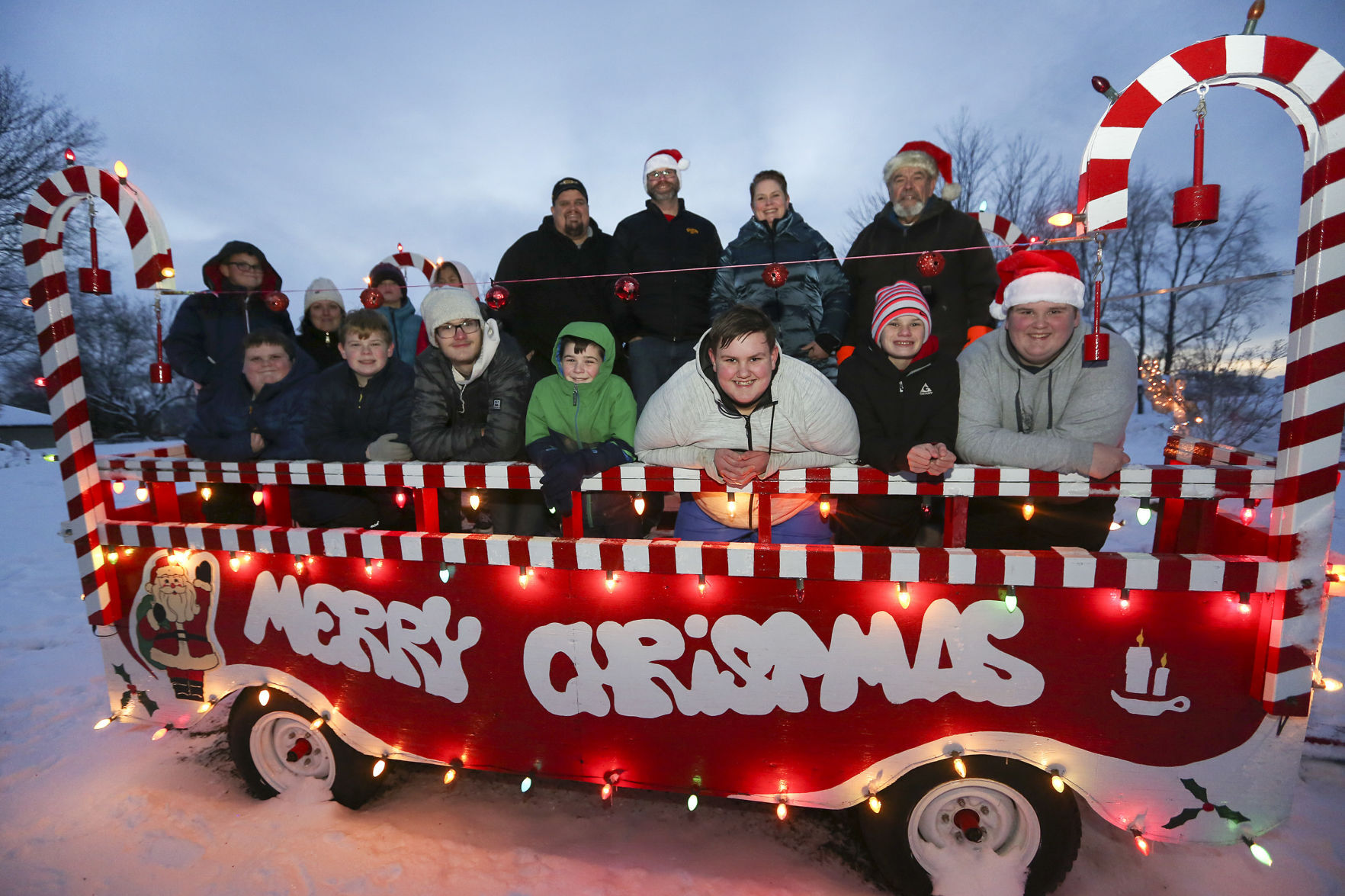 Terry Licht and his family pose for a photo with their Christmas wagon outside his Dubuque home on Tuesday, Dec. 15, 2020. Front, from left: Tate Smith, 12, Teddy Licht, 12, Cole Licht, 16, Oliver Licht, 9, Drew Smith, 13, Wyatt Licht, 12, and Owen Smith, 15. Back, from left: Reed Licht, 11, Sara Licht, Tanner Licht, 8, Emme Smith, 10, Troy Smith, Eli Licht, Courtney (Licht) Smith and Terry Licht. PHOTO CREDIT: NICKI KOHL
