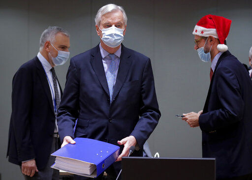 A colleague wears a Christmas hat as European Union chief negotiator Michel Barnier, carries a binder of the Brexit trade deal during a special meeting of Coreper, at the European Council building in Brussels. Four days after sealing a free trade agreement with the European Union, the British government warned businesses to get ready for disruptions and “bumpy moments” when the new rules take effect on Thursday night. PHOTO CREDIT: Olivier Hoslet