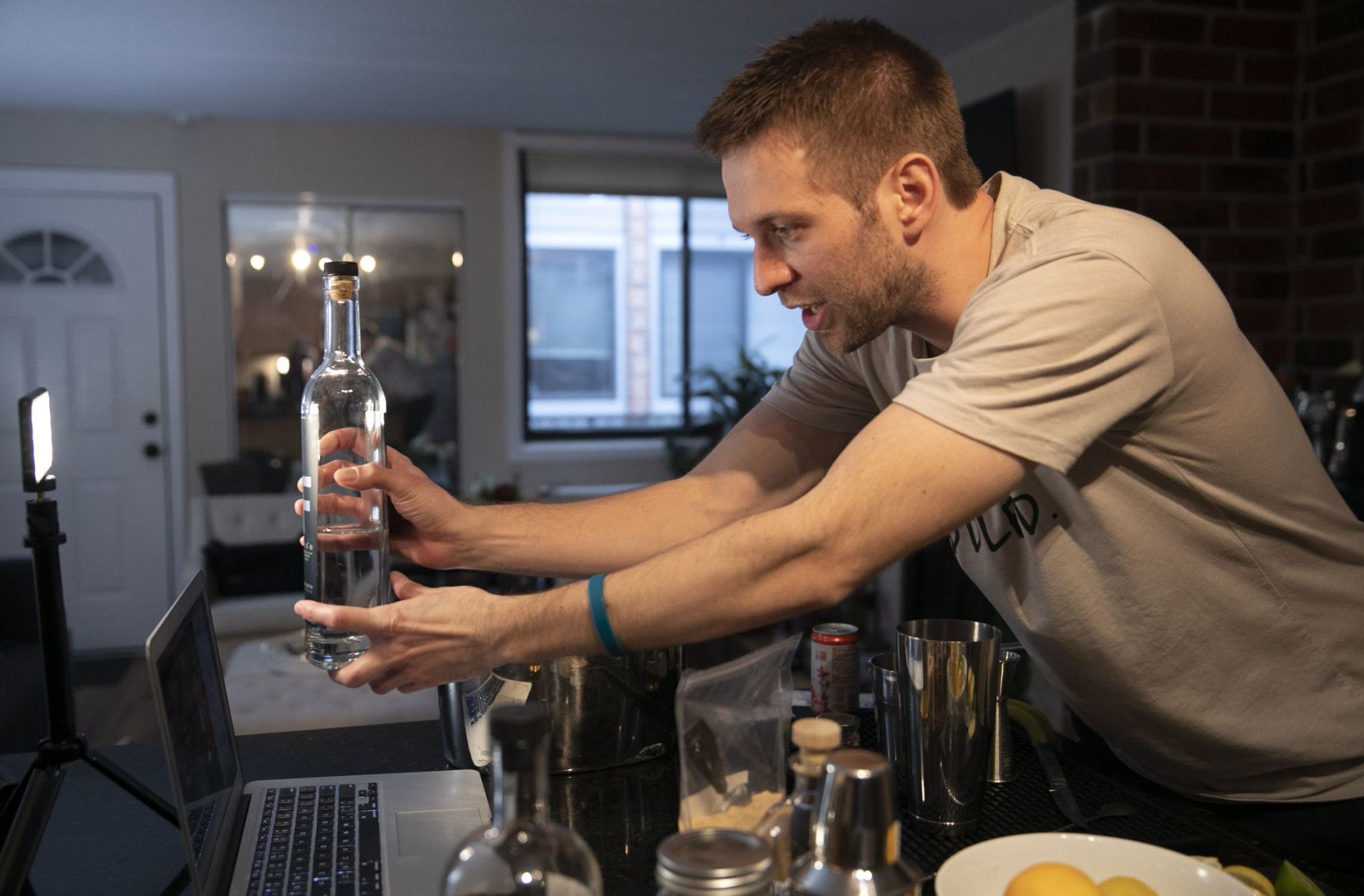 Ross Hunt, owner of unMuddled Bartending Co., brings a bottle of tequila closer to the camera so his class can see during a virtual mixology cocktail class in his apartment. He said that in many ways, the pandemic has allow his business to flourished. PHOTO CREDIT: Tribune News Service