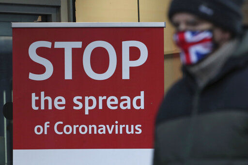 A man wearing a British union flag face mask walks past a coronavirus advice sign outside a bank in Glasgow. Despite growing vaccine access, January is looking grim around the globe as the virus resurges and reshapes itself from Britain to Japan to California. PHOTO CREDIT: Andrew Milligan