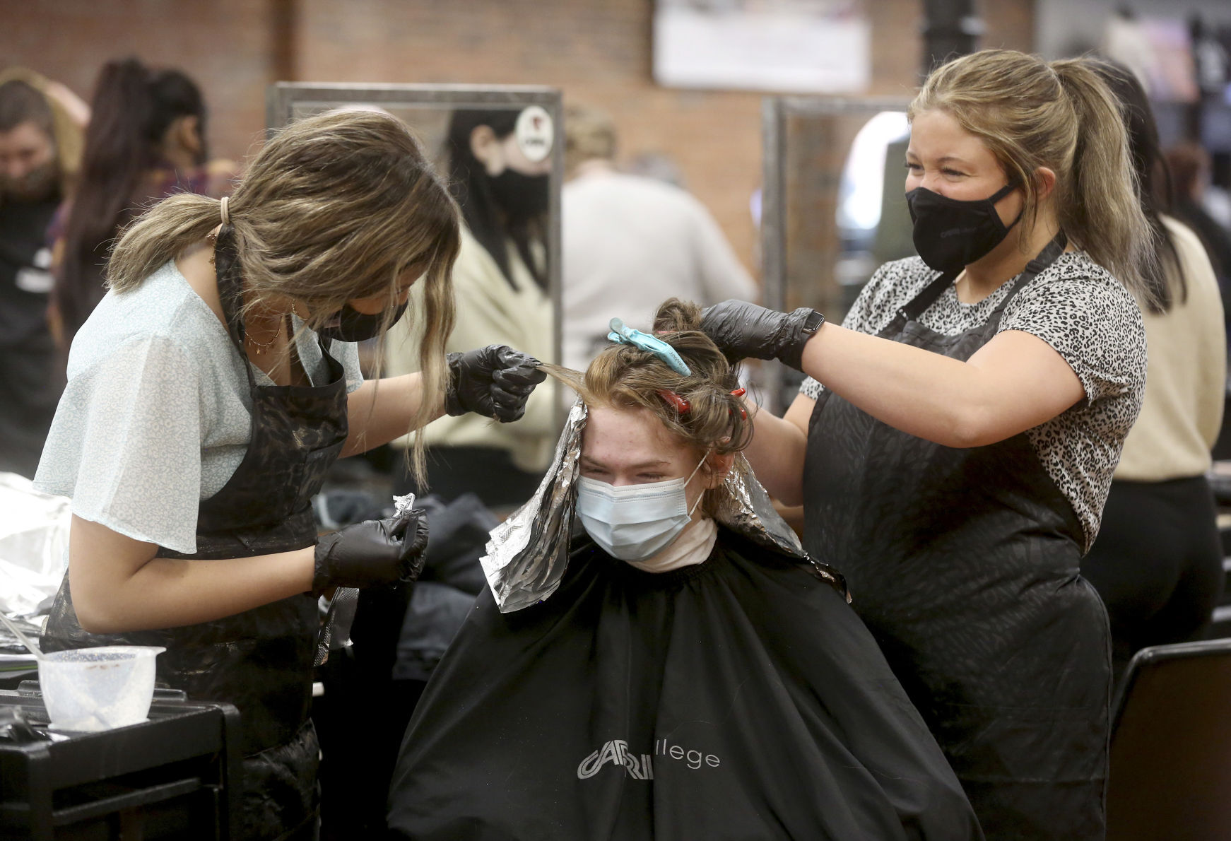 Capri College students Lexie Brandt (left) and Shelby Duehr apply a hair color to Dwight Lloyd, of Hanover, Ill., at Capri in Dubuque on Thursday. PHOTO CREDIT: JESSICA REILLY