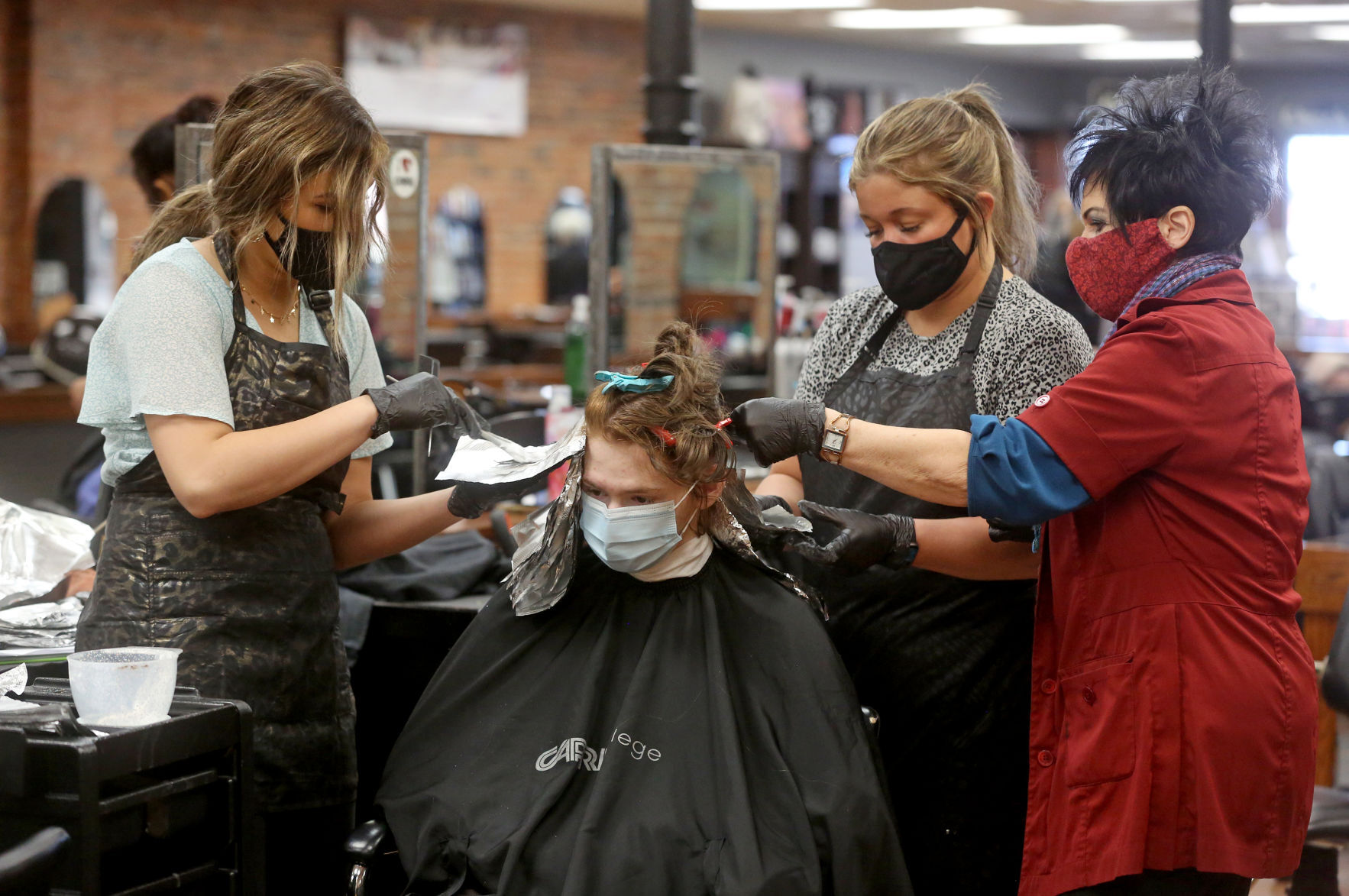 Capri College students Lexie Brandt (left) and Shelby Duehr (second from right) and instructor Diana Bonifas apply a hair color to Dwight Lloyd, of Hanover, Ill., at Capri in Dubuque on Thursday. PHOTO CREDIT: JESSICA REILLY
