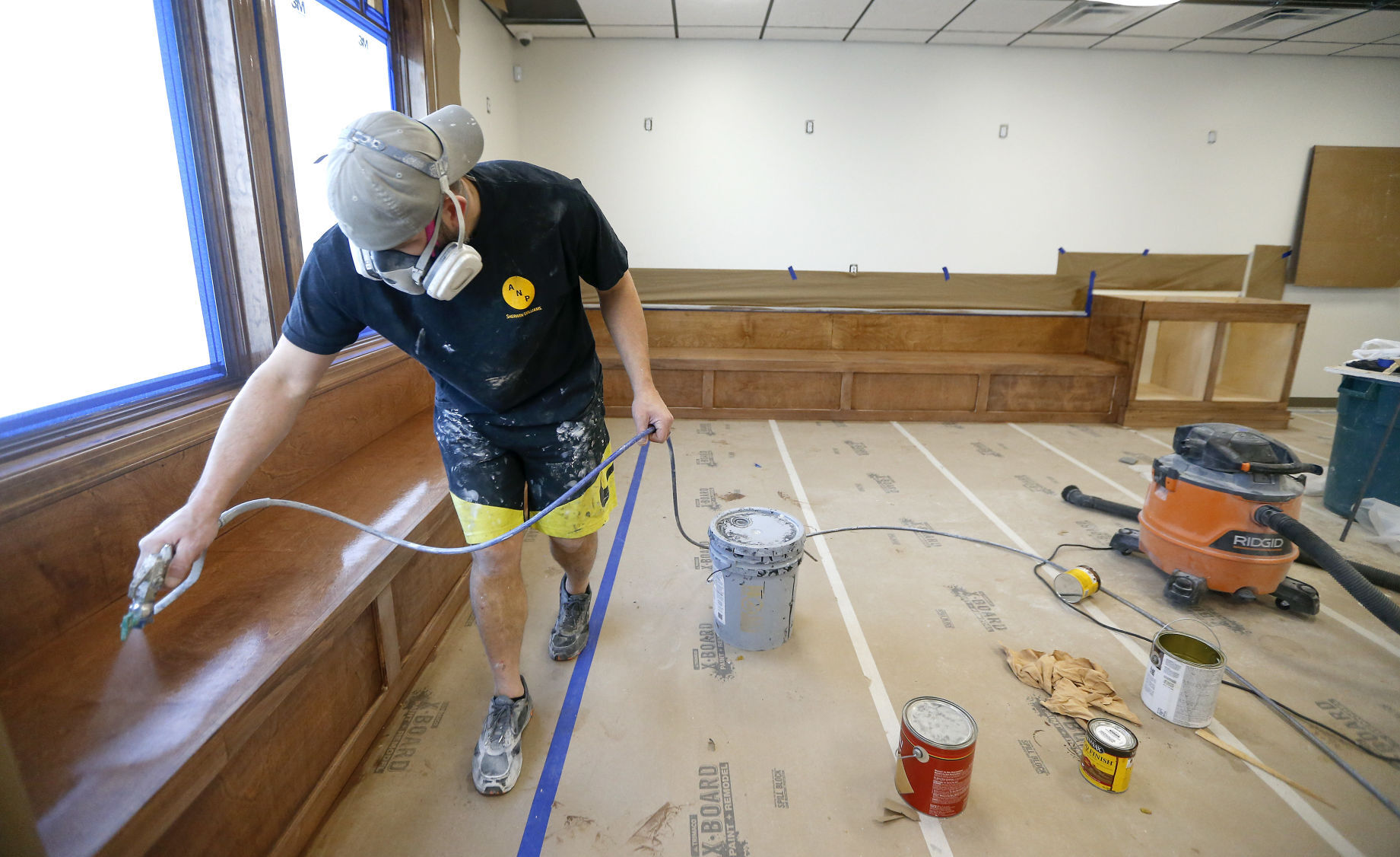 Greg Lehman, of Lehman Painting, sprays lacquer onto wooden seating in the lobby of the future home of an adult-use cannabis dispensary on Illinois 35 in East Dubuque, Ill. PHOTO CREDIT: Dave Kettering