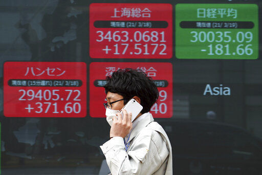 A man wearing a protective mask walks in front of an electronic stock board at a securities firm Friday, March 19, 2021, in Tokyo. Asian stock markets followed Wall Street lower on Friday after rising U.S. bond yields pulled stocks lower, dampening enthusiasm driven by the Federal Reserve