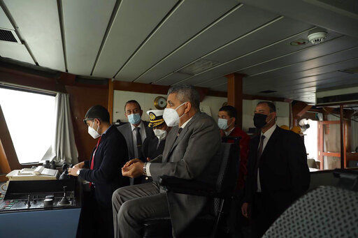 This photo released by the Suez Canal Authority on Thursday, March 25, 2021, shows the head of the Suez Canal Authority, Lt. Gen. Ossama Rabei, center, with a team look from another vessel towards the Ever Given, a Panama-flagged cargo ship, after it become wedged across the Suez Canal. An operation is underway to try to work free the ship, which further imperiled global shipping Thursday as at least 150 other vessels needing to pass through the crucial waterway idled waiting for the obstruction to clear. (Suez Canal Authority via AP) PHOTO CREDIT: HOGP