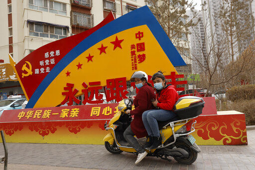 Residents wearing masks pass by government propaganda with slogans some of which read "Forever follow the Party" and "China