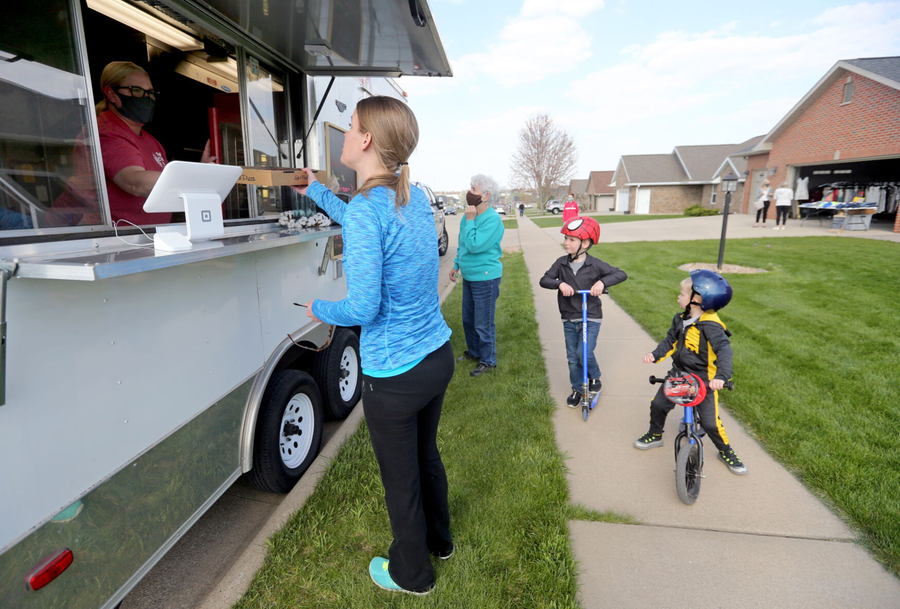 Jennifer Billmeyer gets a pizza from Irene Nelson, co-owner of Town Clock Inn, as Billmeyer’s sons Owen (left), 6, and Oliver, 3, wait outside Amanda Kennedy’s home in Asbury, Iowa, on Thursday. PHOTO CREDIT: JESSICA REILLY