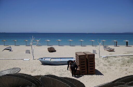 Workers arrange sunbeds as others install umbrellas at Plaka beach on the Aegean island of Naxos, Greece, Wednesday, May 12, 2021. With debts piling up, southern European countries are racing to reopen their tourism services despite delays in rolling out a planned EU-wide travel pass. Greece Friday became the latest country to open up its vacation season as it dismantles lockdown restrictions and focuses its vaccination program on the islands. (AP Photo/Thanassis Stavrakis) PHOTO CREDIT: Thanassis Stavrakis