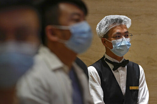 A worker wearing a face mask and a hair net to help curb the spread of the coronavirus stands near masked reporters during a press conference in Beijing, Tuesday, May 25, 2021. (AP Photo/Andy Wong) PHOTO CREDIT: Andy Wong
