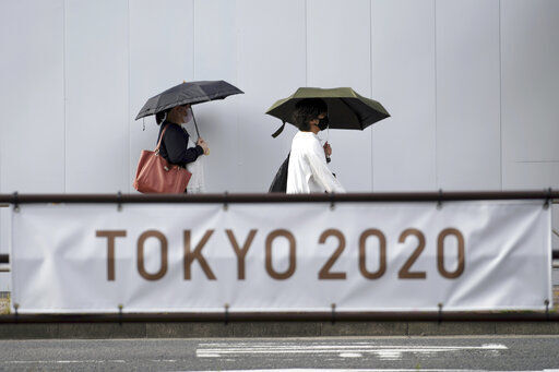 People wearing masks to help protect against the spread of the coronavirus walk near a banner to promote the Tokyo Olympic Games Tuesday, May 25, 2021, in Tokyo. (AP Photo/Eugene Hoshiko) PHOTO CREDIT: Eugene Hoshiko
