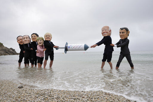 Activists wearing giant heads of the G7 leaders tussle over a giant COVID-19 vaccine syringe during an action of NGO