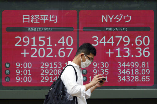 A man wearing a protective mask walks in front of an electronic stock board showing Japan