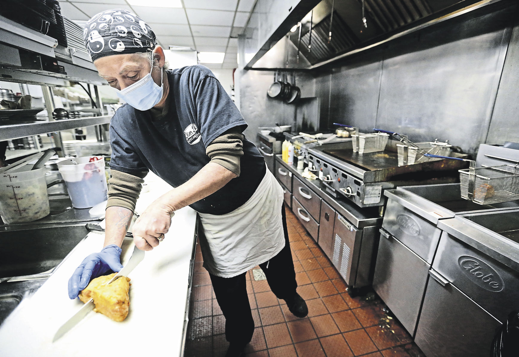 Tammy Hammel cuts a sandwich while preparing practice meals for Bennigan’s On the Fly at Holiday Inn in Dubuque in February. It participates in a trend called ghost kitchen, where a restaurant prepares food from a variety of other restaurants.    PHOTO CREDIT: JESSICA REILLY