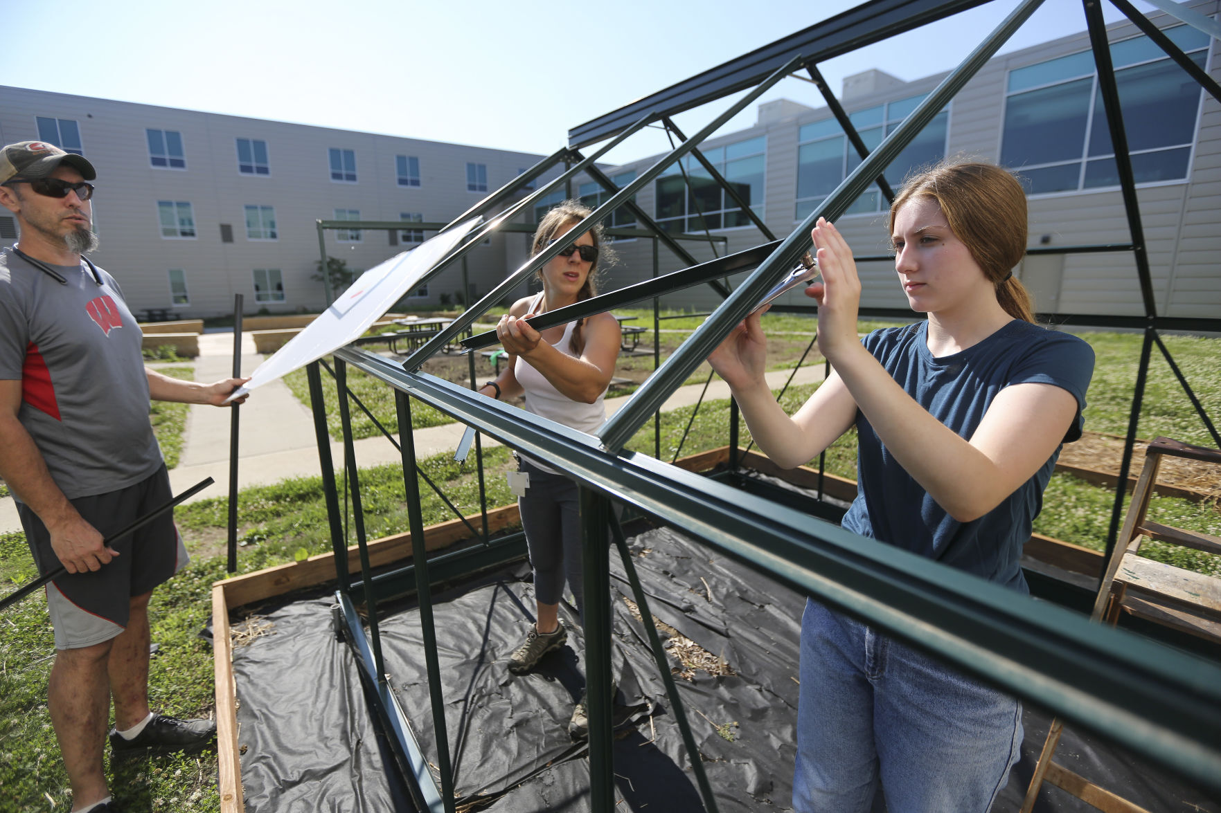 Wahlert Catholic High School junior Megan Hefel (right), 16, helps construct a greenhouse last week with instructor Korrin Schriver and Schriver’s husband, Sean.    PHOTO CREDIT: Dave Kettering