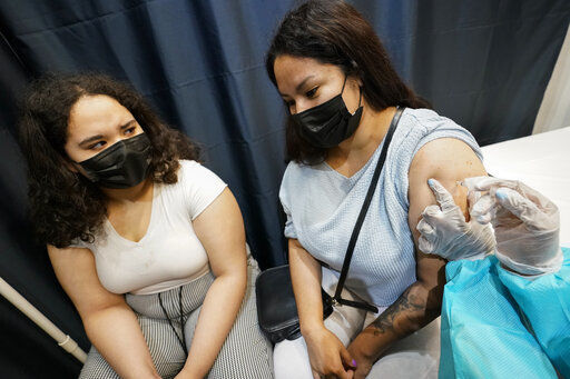 A health care worker inoculates Evelyn Pereira (right), of Brooklyn, with the first dose of the Pfizer COVID-19 vaccine as her daughter Soile Reyes, 12, looks on. New York City will require all of its municipal workers — including teachers and police officers — to get coronavirus vaccines by mid-September or face weekly COVID-19 testing, Mayor Bill de Blasio announced today.    PHOTO CREDIT: Mary Altaffer