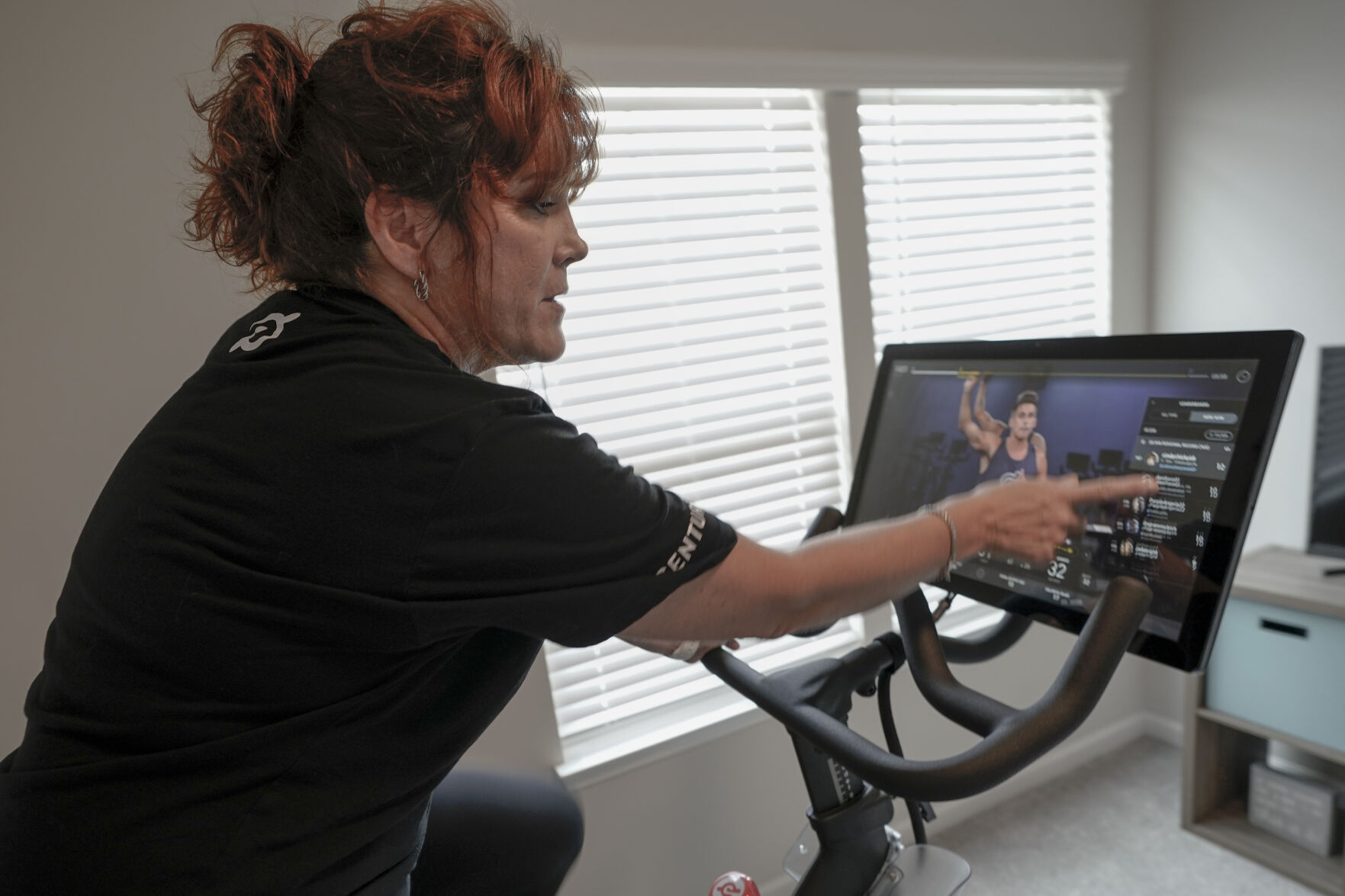 Cindy Cicchinelli, points out others on the screen listed to be cycling at the same time as she watches the online video while using her Peloton exercise machine in the workout room of her Pittsburgh townhouse. Cicchinelli says she has become a dedicated Peloton user after going to her gym in Pittsburgh for years, she said the convenience is what has sold her. The pandemic is reshaping America