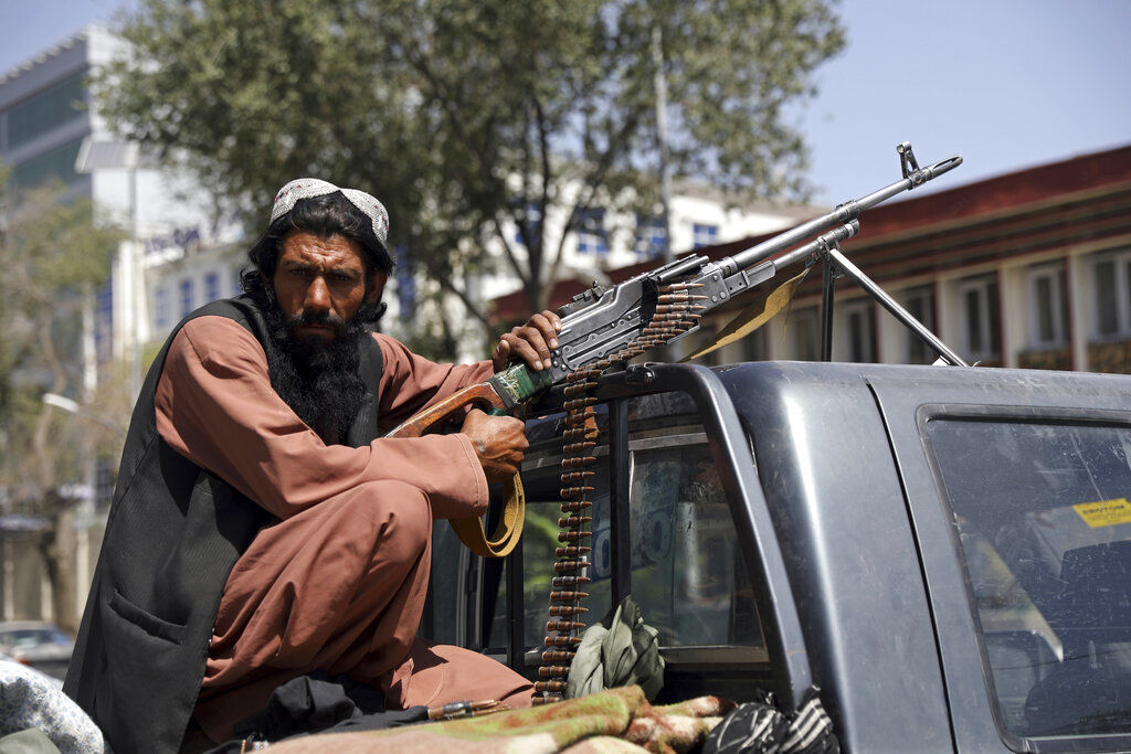A Taliban fighter sits on the back of a vehicle with a machine gun in front of the main gate leading to the Afghan presidential palace, in Kabul, Afghanistan. Thousands of Afghans rushed onto the tarmac of Kabul