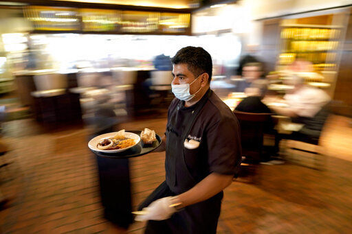 Marcelino Flores wears a face mask as he delivers food to a table at Picos restaurant in Houston. Half of American workers are in favor of vaccine requirements at their workplaces, according to a new poll, as such mandates gain traction following the U.S. government’s full approval to Pfizer’s COVID-19 vaccine.     PHOTO CREDIT: David J. Phillip