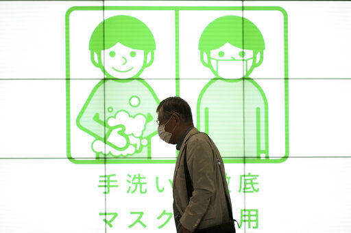 A man walks past a public awareness sign for wearing protective masks and washing hands to help reduce the spread of the coronavirus in Tokyo. The World Health Organization reported that the global number of new coronavirus cases and deaths continued to fall in the past week, with an estimated 3.3 million new infections and about 55,000 deaths, marking a 10% drop in both.    PHOTO CREDIT: Eugene Hoshiko