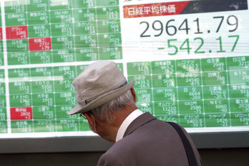 A man wearing a protective mask looks at an electronic stock board showing Japan