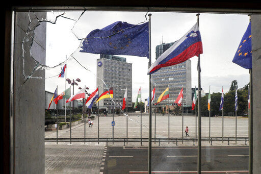 Slovenian and EU flags are seen through a window of the parliament building, in Ljubljana, Thursday, Sept. 16, 2021, broken by anti-COVID measures protesters the previous night. Slovenia has introduced a mandatory anti-COVID vaccination for all civil service employees, further tightening anti-coronavirus measures that have triggered a major riot in the small Alpine state. The measure passed Friday Sept. 17, 2021 says that all state administration employees will need to be vaccinated with one shot by Oct. 1 and by Nov. 1 with the second, unless it
