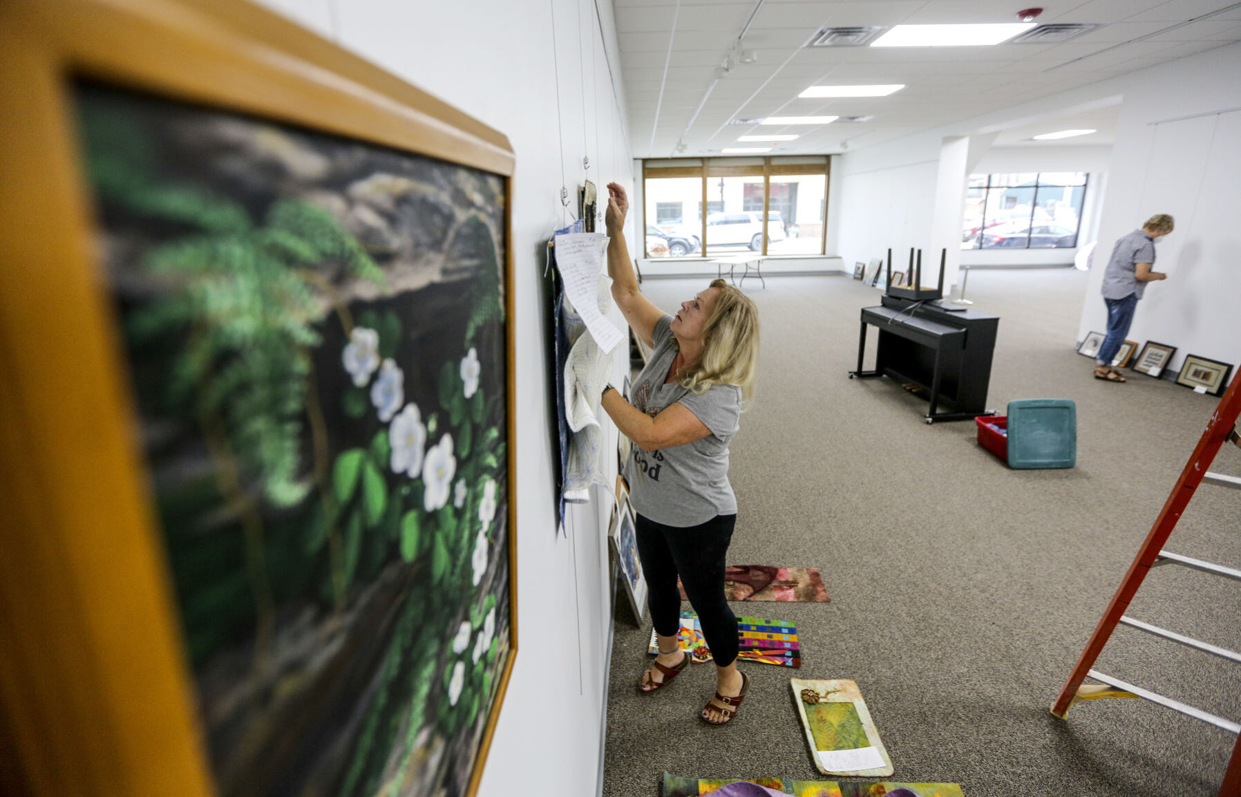 Volunteers Barb Bowman (left) and Helen Zabel hang up artwork inside the newly-renovated Maquoketa Art Experience, which shares a building with Maquoketa Chamber of Commerce, on Tuesday. The nonprofits reopened to the public this week.    PHOTO CREDIT: Dave Kettering