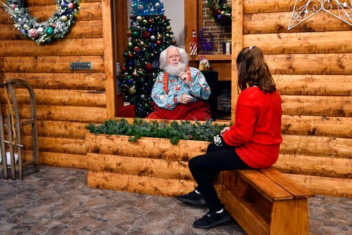 Santa, Sid Fletcher, sits behind a glass barrier as he hears Kendra Alexander of St. James, Minn., during her visit Monday, Nov. 15, 2021, at The Santa Experience at the Mall of America in Bloomington, Minn. Where allowed, some malls and big-box stores are offering Santa