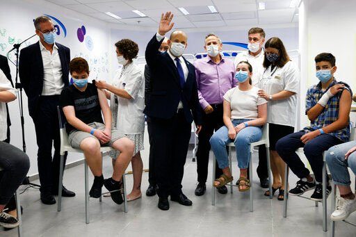 FILE - Israeli Prime Minister Naftali Bennett, center, gestures as he stands next to youths during his visit to a Maccabi healthcare maintenance organisation (HMO) outlet which offers vaccinations against the coronavirus disease (COVID-19) in Holon, near Tel Aviv, Israel Tuesday, June 29, 2021. The coronavirus