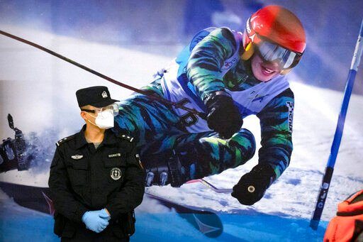 A police officer wearing a face mask and goggles to protect against COVID-19, stands near a poster of a skier on the wall at a train station in Zhangjiakou in northern China