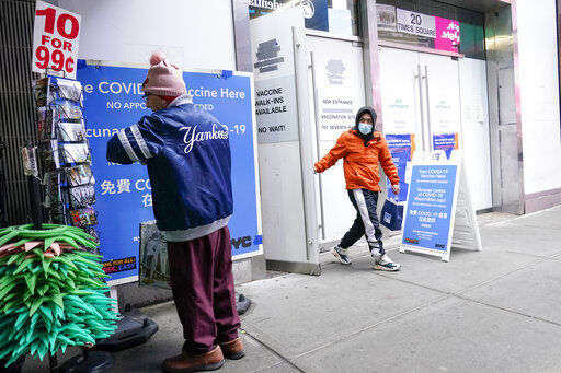 A man, right, leaves a NYC vaccine hub as another shops for postcards at a souvenir shop in New York